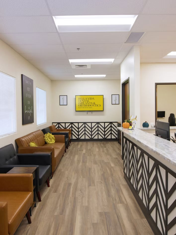 The image shows an interior space with a modern design, featuring a waiting area with seating, a reception desk, and decorative elements such as wall art and a sign that reads The Wellness Center.