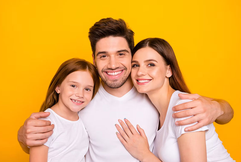 A family of four posing together against a yellow background with smiles on their faces.